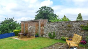 Une terrasse avec une table et des chaises en pierre, un barbecue et un mur en pierre.