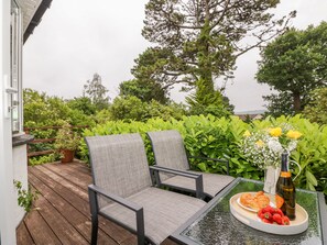 Un balcon avec une table en verre, deux chaises grises et une assiette de fraises et de croissants.