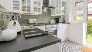 A modern kitchen with white cabinets, a black stove, and a window with a view of greenery. - Hilltop (Totnes)