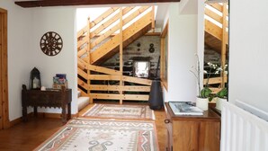 A room with a sloped wooden ceiling, a wooden staircase, a patterned rug, a small cabinet, and a radiator. - Cardean Mill (Blairgowrie)
