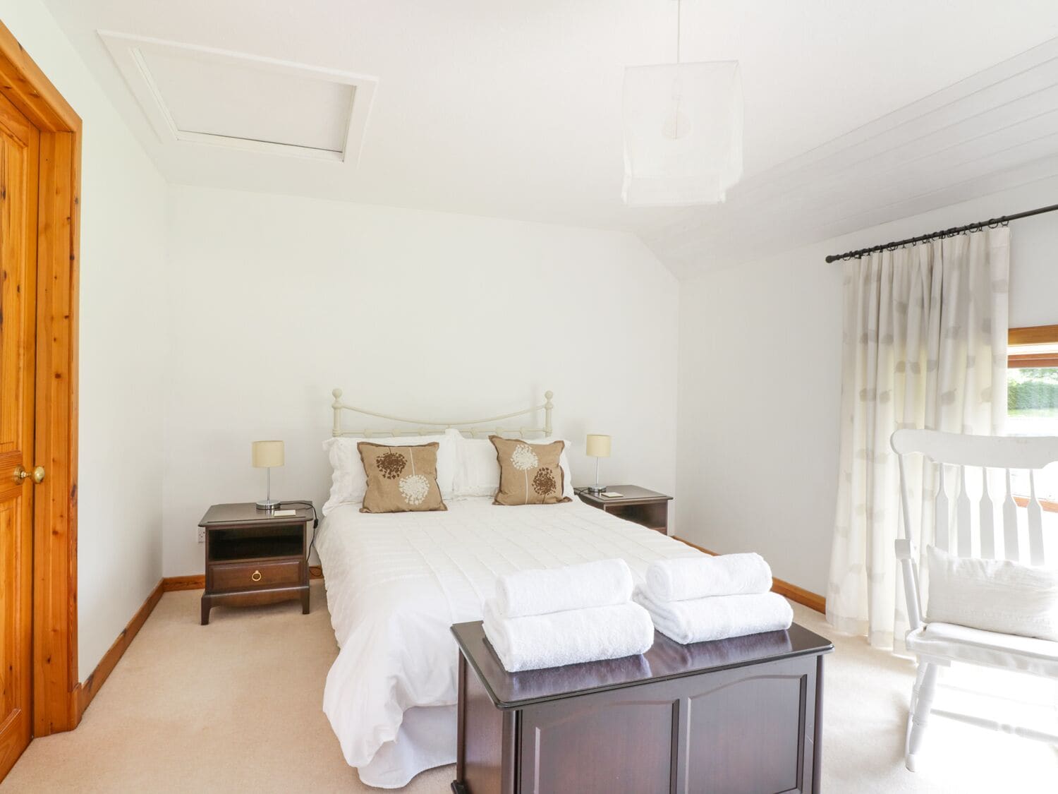 A bedroom with a bed, bedside tables, a wooden wardrobe, a chair, and a window with curtains.