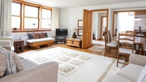 A spacious living room with a sofa, a TV, and a dining area with wooden furniture. - Cardean Mill (Blairgowrie)