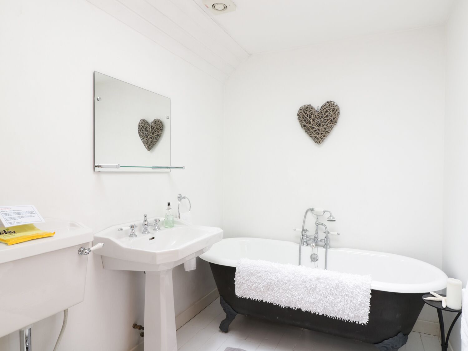 A bathroom with a white sink, a black bathtub, and two heart-shaped wall decorations.