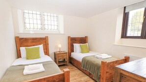A room with two wooden beds, a nightstand with a lamp, and a window with a grid design. - Andlestone (Matlock)