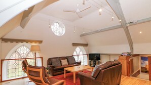 A spacious loft-style living room with a high ceiling, wooden floors, a leather sofa, a wooden coffee table, and a TV. - Andlestone (Matlock)