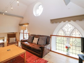 Una sala de estar acogedora con un sofá de cuero, una mesa de madera y un tapete rojo. Hay una ventana con un diseño de vitral y un tragaluz circular.