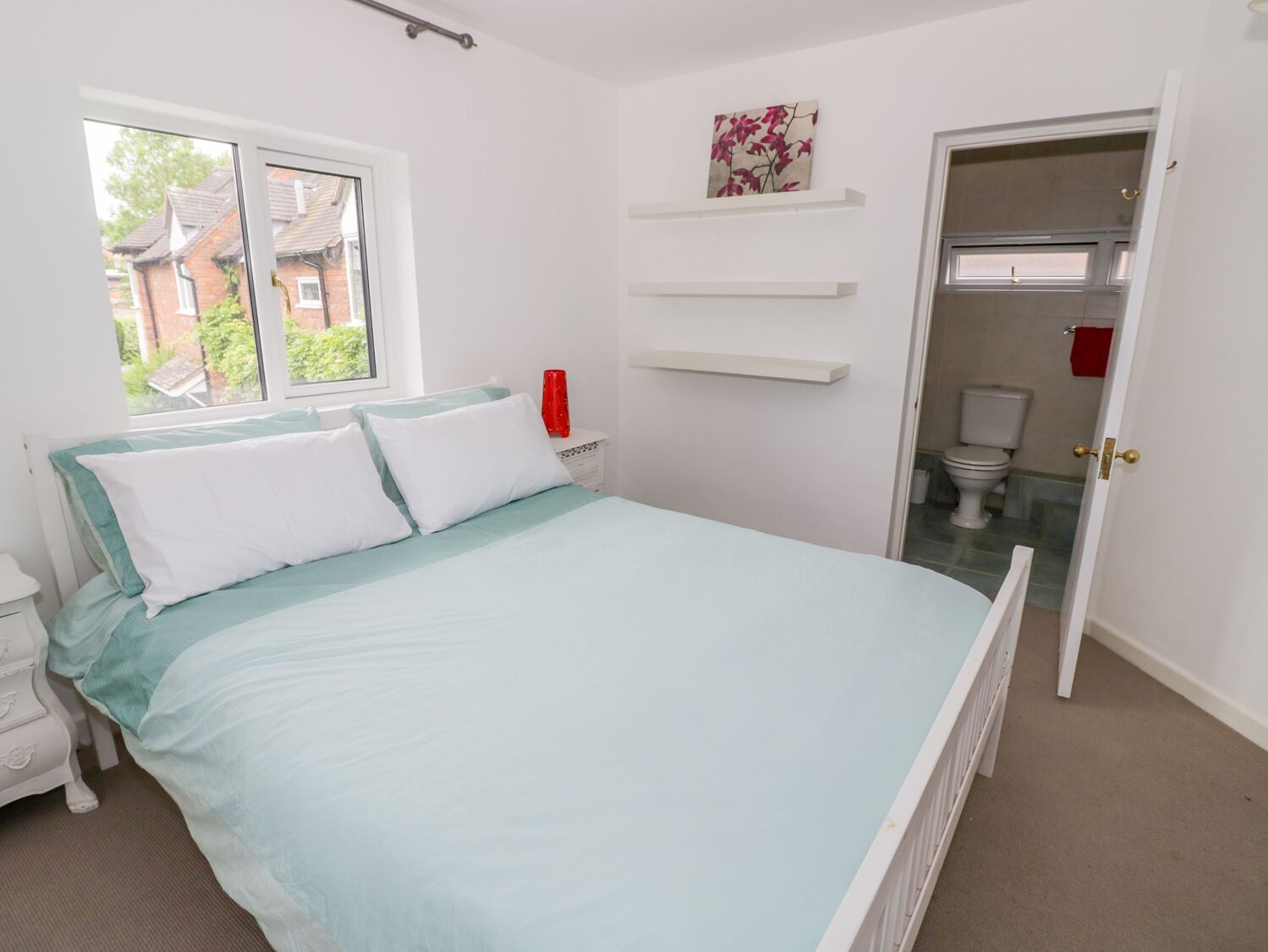 A bedroom with a bed, a nightstand, a window, and a door leading to a bathroom.
