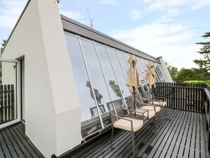 A modern outdoor deck with a glass enclosure, metal chairs, and umbrellas.