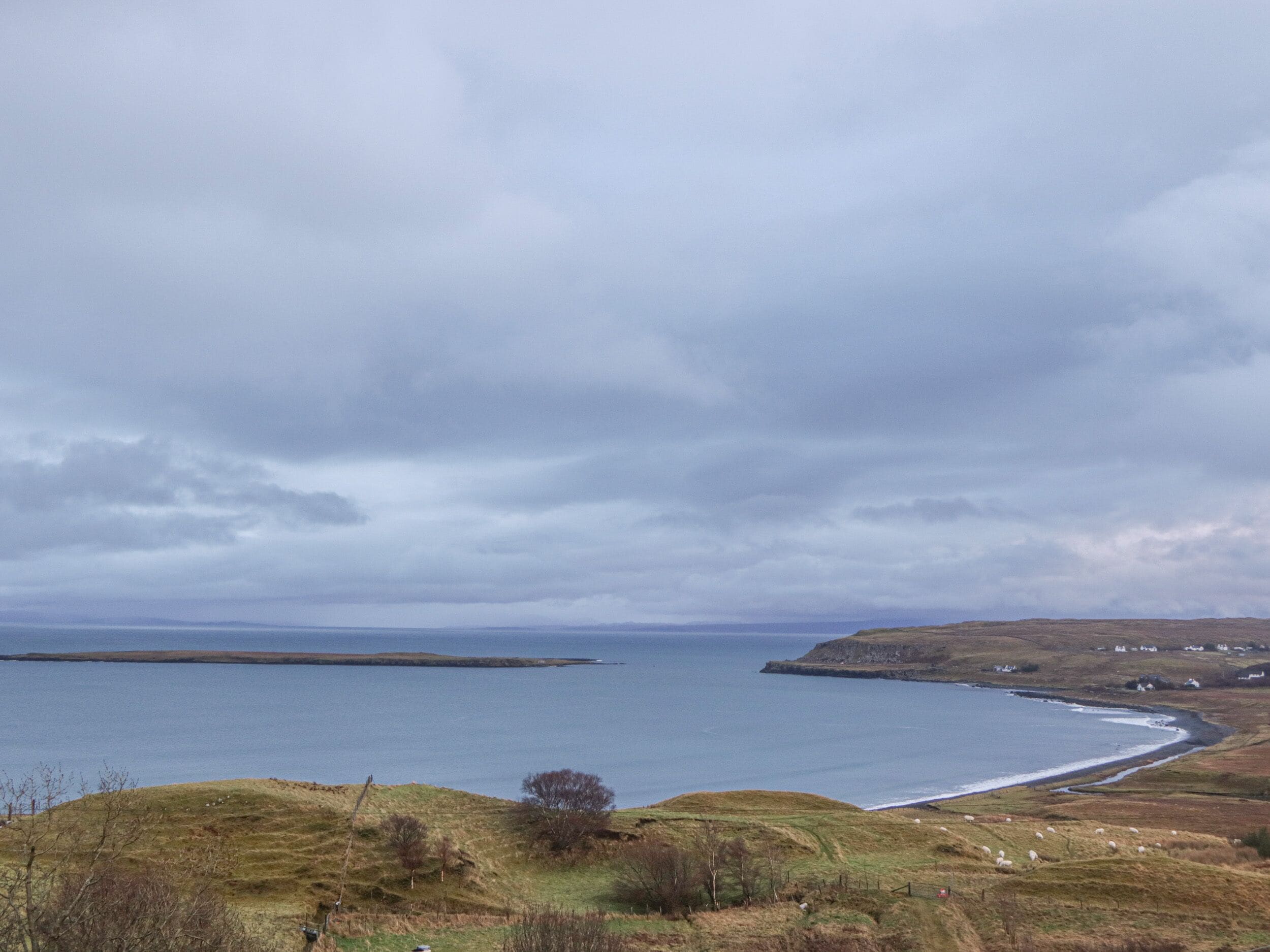 A coastal landscape with a body of water, grassy hills, and a few scattered houses.