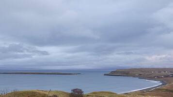 A coastal landscape with a body of water, grassy hills, and a few scattered houses.