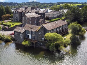 A stone building with multiple windows and a balcony, situated by a river. - Pennington (Ambleside)