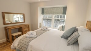 Un dormitorio con cama, mesita de noche, espejo y ventana con vistas a árboles y agua.