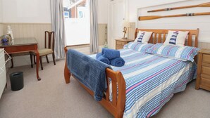 A bedroom with a bed, a desk, a chair, a lamp, and a window with curtains. - Lancaster House (Sandown)