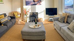 A living room with two grey sofas, a coffee table, a fireplace, a flat-screen TV, and a large window with a view of the beach. - Quayside (Whitby)