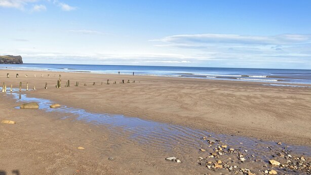 A beach with a clear sky, calm sea, and a rocky shoreline. - Quayside (Whitby)