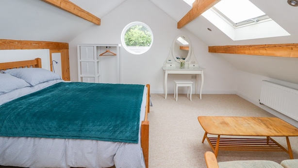 A bedroom with a skylight, a bed, a vanity, and a small table. - The Stables (Frodsham)