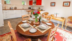 A dining area with a round wooden table set for four, surrounded by wicker chairs. A vase with flowers and a bottle of champagne are on the table. - The Stables (Frodsham)