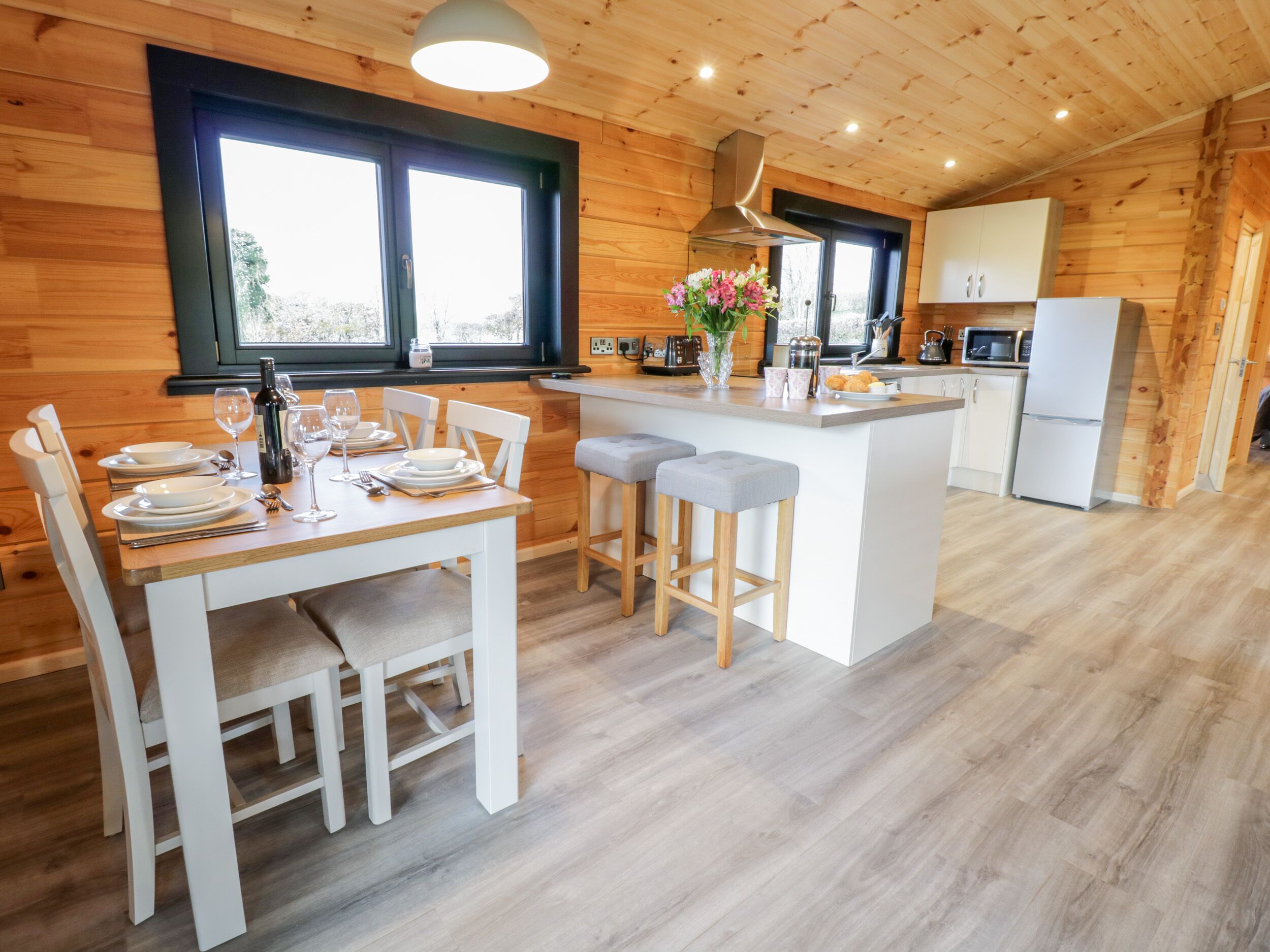 A modern kitchen with wooden walls, a central island, and a dining area with white furniture.