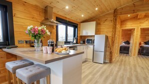 A modern kitchen with wooden walls, a central island with bar stools, a refrigerator, and a microwave. - Bryn Eiddon Log Cabin (Machynlleth)