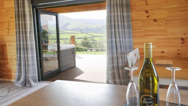A wooden interior with a table, a bottle of wine, and two glasses. - Bryn Eiddon Log Cabin (Machynlleth)
