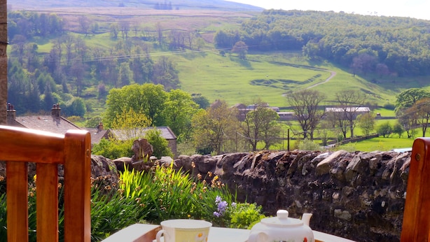 A wooden table with a teapot and cup, overlooking a green valley with fields and a stone wall. - Dale View (Skipton)