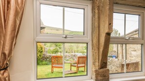 A room with a large window overlooking a garden with a wooden bench and a stone wall. - Dale View (Skipton)