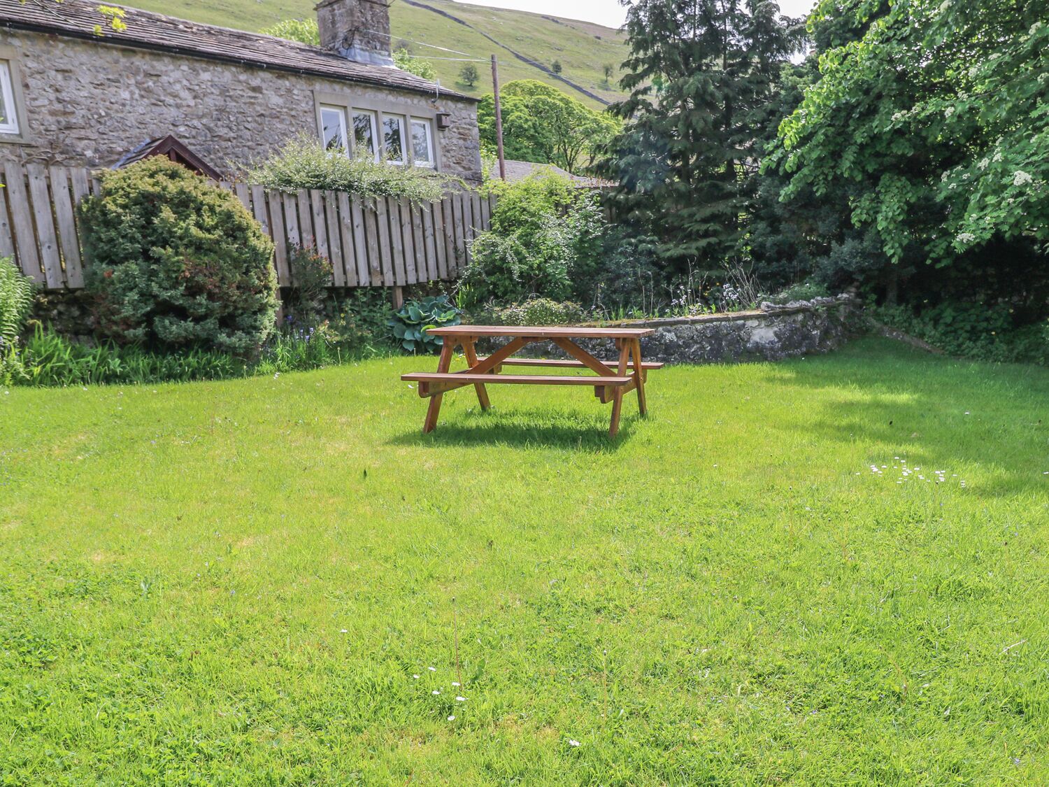 Et stenhus med plankeværk og et picnicbord i en græsplæne.