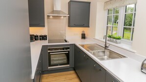 A compact kitchen with a built-in oven, a sink, and a window with a view of greenery. - Ryedale Country Lodges - Hazel Lodge (York)
