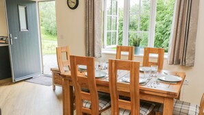 A dining area with a wooden table set for four, surrounded by chairs with plaid cushions. A clock is mounted on the wall above the table. - Ryedale Country Lodges - Hazel Lodge (York)
