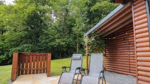 A wooden cabin with a patio area featuring two lounge chairs and a wooden bench. - Ryedale Country Lodges - Hazel Lodge (York)