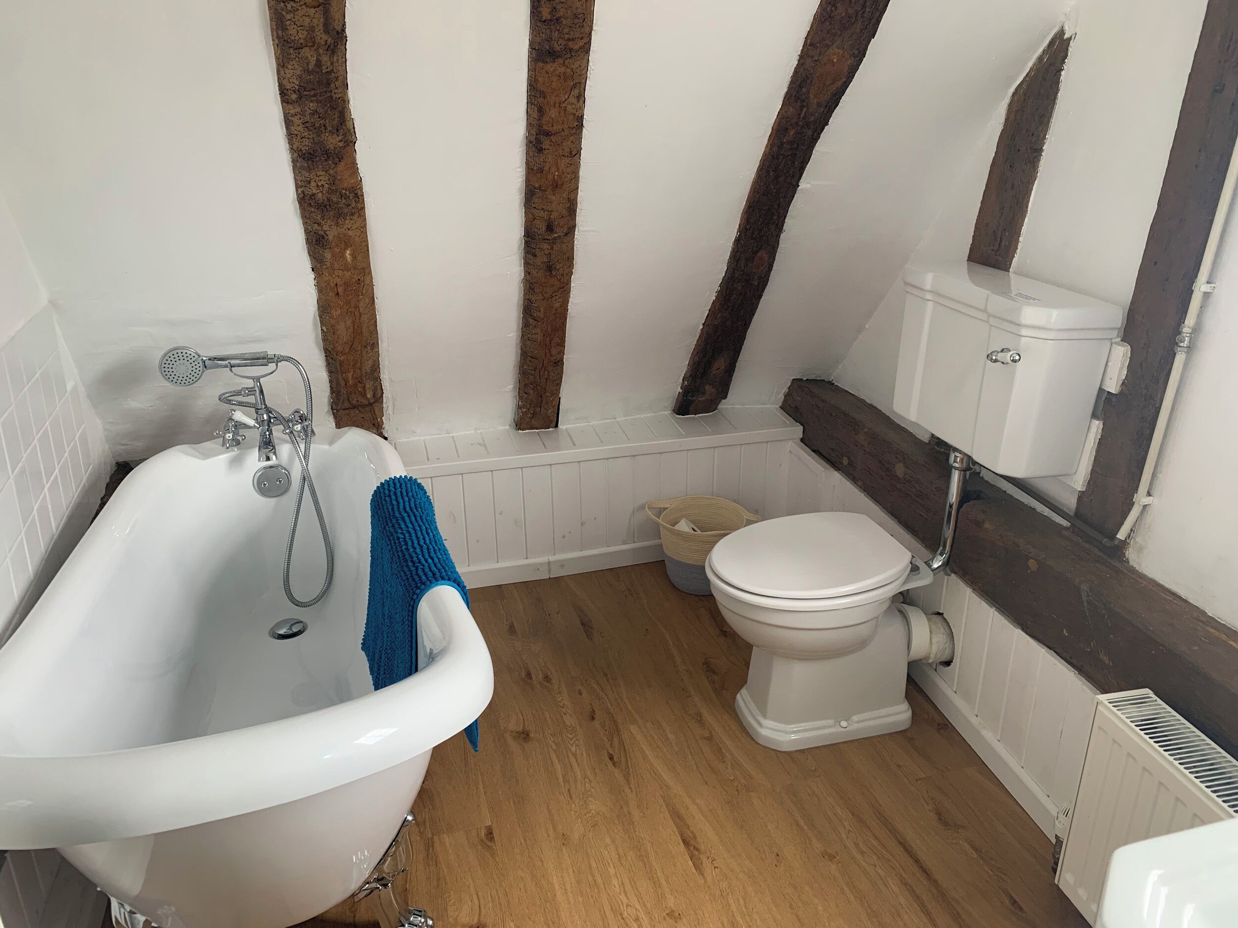 A bathroom with a white bathtub, a white toilet, and a wooden floor.