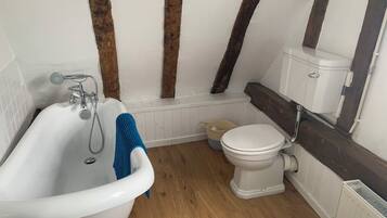 A bathroom with a white bathtub, a white toilet, and a wooden floor.