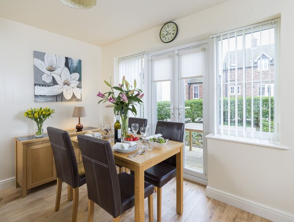 A dining area with a wooden table, chairs, a vase with flowers, and a clock on the wall.