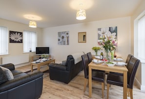 A modern living room with a sofa, a dining table set for four, and a television.