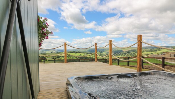 Ein Whirlpool mit Holzboden und Seilsperrung mit Blick auf eine schöne Landschaft, mit Hügeln und blauem Himmel.