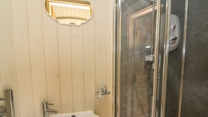 Ein Badezimmer mit einem weißen Waschbecken, einer Duschkabine aus Glas und einer wandmontierten Leuchte.