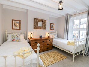 A bedroom with two beds, a wooden dresser, and a large window with curtains. - Rosie Cottage (Filey)
