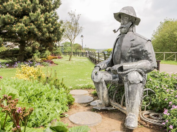 A statue of a seated man with a pipe, surrounded by a garden with various plants and flowers. - Rosie Cottage (Filey)