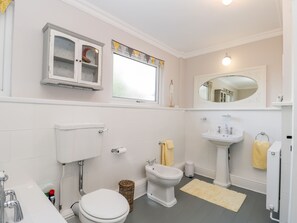 A bathroom with a toilet, bidet, sink, and a cabinet above the toilet. - Rosie Cottage (Filey)