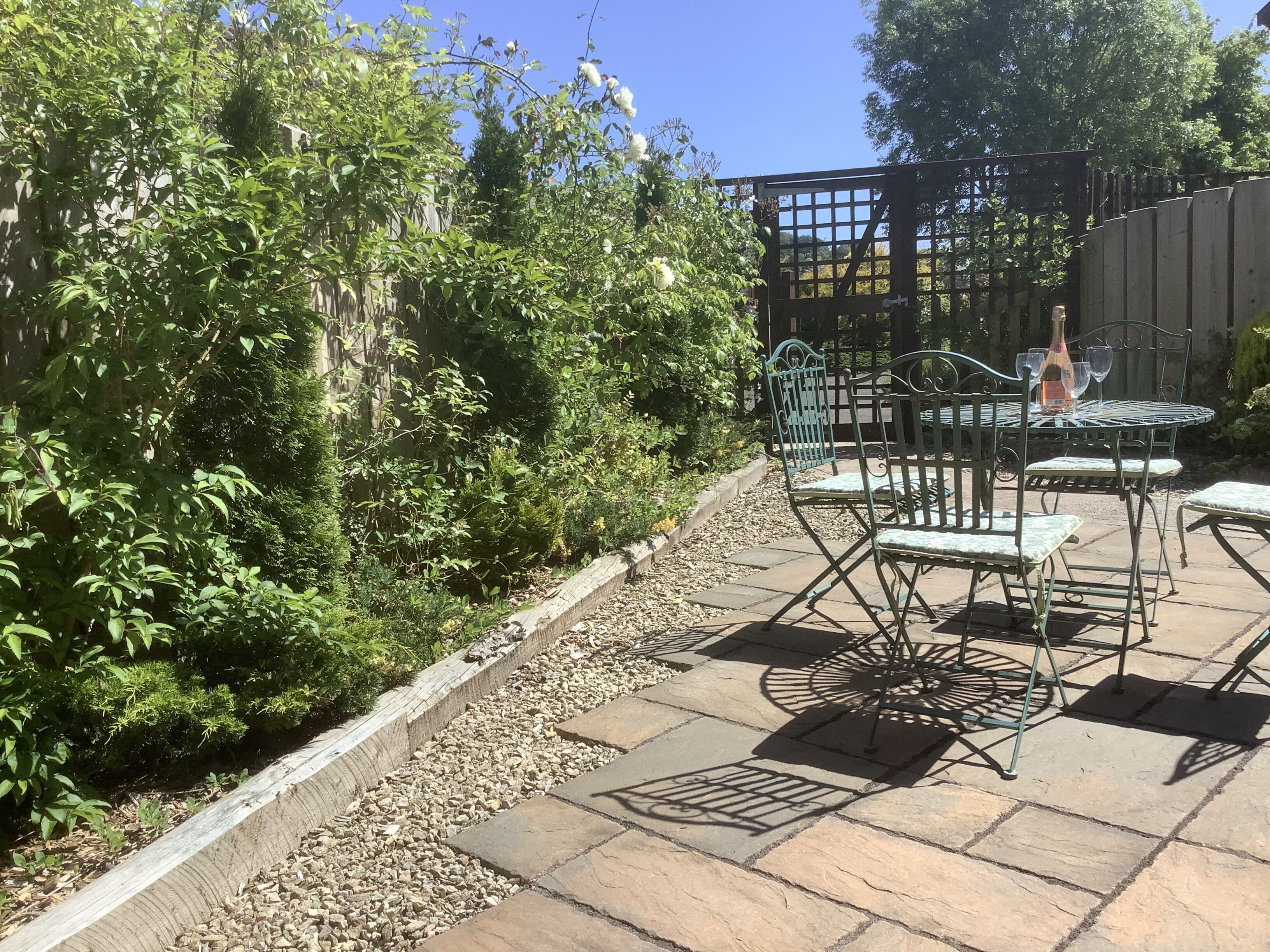 Een terras buiten met stenen vloer, metalen stoelen en een tafel.