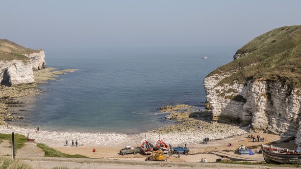 A coastal beach with cliffs, a rocky shoreline, and a small boat docked near the shore. - Chalkstone Cottage (Bridlington)