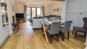 A dining area with a wooden floor, a glass table, and grey upholstered chairs. - Chalkstone Cottage (Bridlington)