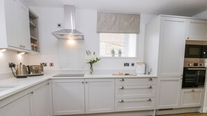 A modern kitchen with white cabinetry, a stainless steel range hood, a window with a view, and a built-in oven. - Chalkstone Cottage (Bridlington)