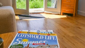 Una revista sobre una mesa en una habitación con piso de madera, un sofá y una televisión sobre un mueble de madera.