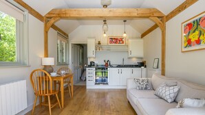 Un interior acogedor con una mesa de comedor de madera, un sofá y una zona de cocina con armarios blancos y luces colgantes.