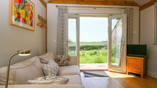 Una sala de estar acogedora con un sofá, una lámpara, un televisor y vistas a un paisaje verde a través de una puerta de cristal.