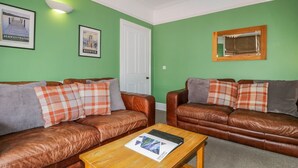 A living room with two brown leather sofas, a wooden coffee table, and green walls. - Sefton House (Keswick)