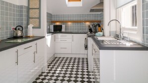 A compact kitchen with a checkered floor, white cabinets, a microwave, and a sink. - Sefton House (Keswick)