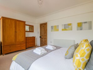 A bedroom with a large wooden wardrobe, a bed with a grey and yellow patterned bedspread, and three abstract paintings on the wall. - Sefton House (Keswick)