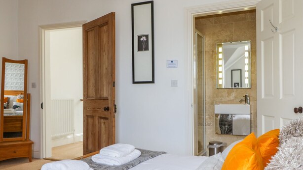 A hotel room with a bed, a wooden door, a bathroom with a mirror, and a towel rack. - Sefton House (Keswick)